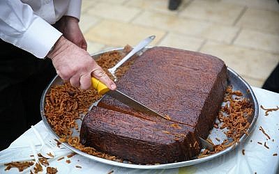 Illustrative. An ultra-Orthodox man cuts kugel during Rosh Hodesh (new Jewish month) prayer at the Rashbi gravesite in Meron, Northern Israel on January 17, 2018. (David Cohen/Flash90)
