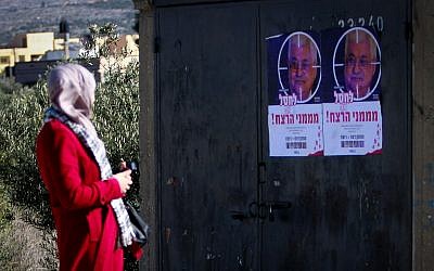 A Palestinian woman walks next to posters showing Palestinian President Mahmoud Abbas with a text reading "eliminate the sponsers of murder" at the Hawara checkpoint, south of the West Bank city of Nablus on December 11, 2018. (Nasser Ishtayeh/Flash90)