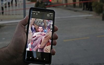 An Israeli settler shows a picture on his cellphone of a Palestinian who attempted a stabbing attack as he is taken away by Israeli soldiers, at the entrance of the Givat Avot neighborhood in the West Bank settlement of Kiryat Arba, on January 11, 2019. (Hazem Bader/AFP)