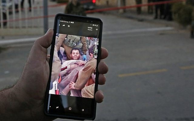 An Israeli settler shows a picture on his cellphone of a Palestinian who attempted a stabbing attack as he is taken away by Israeli soldiers, at the entrance of the Givat Avot neighborhood in the West Bank settlement of Kiryat Arba, on January 11, 2019. (Hazem Bader/AFP)