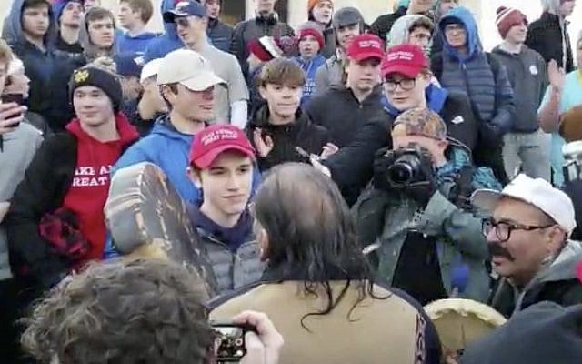 In this January 18, 2019 image made from video provided by the Survival Media Agency, a teenager wearing a "Make America Great Again" hat, center left, stands in front of an elderly Native American singing and playing a drum in Washington. (Survival Media Agency via AP) In this January 18, 2019 image made from video provided by the Survival Media Agency, a teenager wearing a "Make America Great Again" hat, center left, stands in front of an elderly Native American singing and playing a drum in Washington. (Survival Media Agency via AP)