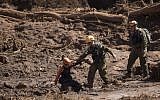 A Brazilian firefighter, left, helps an Israeli rescue specialist to cross a muddy area as they arrive at a site where a person found dead person inside a vehicle stuck in the mud, days after a dam collapse in Brumadinho, Brazil, Monday, Jan. 28, 2019. (AP/Leo Correa)