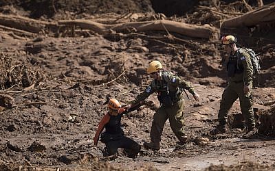 A Brazilian firefighter, left, helps an Israeli rescue specialist to cross a muddy area as they arrive at a site where a person found dead person inside a vehicle stuck in the mud, days after a dam collapse in Brumadinho, Brazil, Monday, Jan. 28, 2019. (AP/Leo Correa)