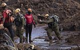 An Israeli rescue specialist, right, arrives at a site where a body was found inside a vehicle stuck in the mud, days after a dam collapse in Brumadinho, Brazil, Monday, Jan. 28, 2019. Firefighters on Monday carefully moved over treacherous mud, sometimes walking, sometimes crawling, in search of survivors or bodies four days after a dam collapse that buried mine buildings and surrounding neighborhoods with iron ore waste. (AP Photo/Leo Correa)