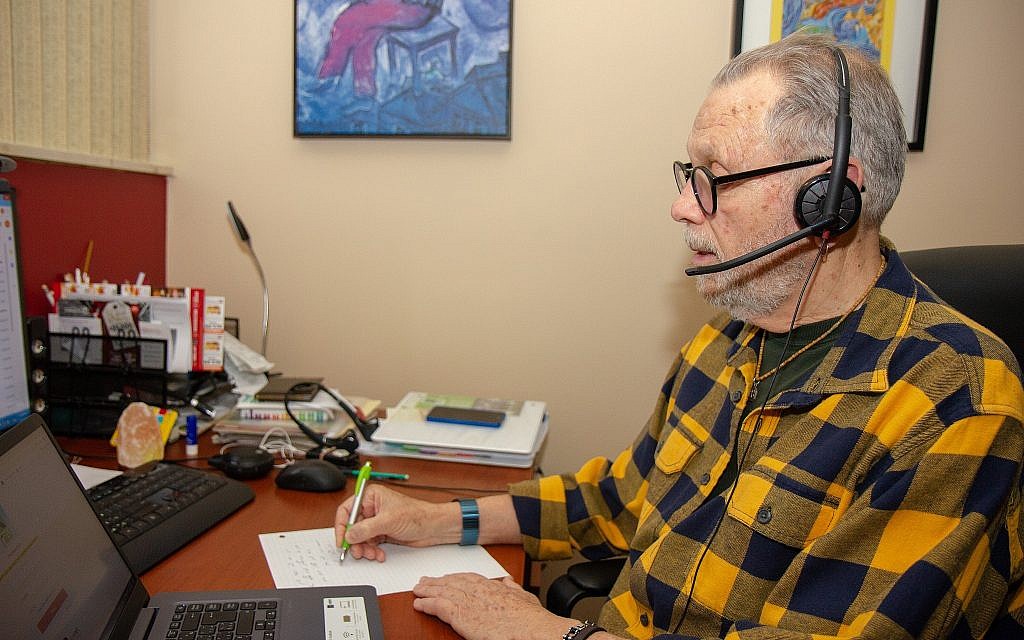 ERAN volunteer Arie Eigner in his apartment, where he receives calls on his laptop. Volunteers take notes during calls for report they must prepare after each call, which they send to their supervisor in Israel. (Etye Sarner)