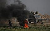 A Palestinian protester runs near burning tires during a demonstration near the fence along the border with Israel, east of Gaza City, on February 15, 2019. An Israeli military vehicle is pictured on the other side of the fence. (Said Khatib/AFP)