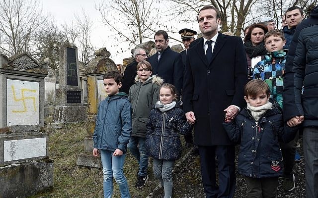 French President Emmanuel Macron holds children by the hands as he visit the vandalized Jewish cemetery in Quatzenheim, eastern France, Tuesday, February 19, 2019. (Frederick Florin, Pool via AP)