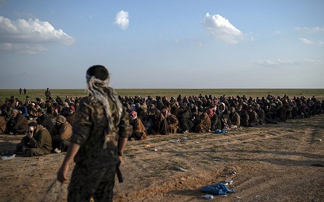 US-backed Syrian Democratic Forces (SDF) fighters stand guard next to men waiting to be screened after being evacuated out of the last territory held by Islamic State militants, near Baghouz, eastern Syria, Friday, Feb. 22, 2019. (AP/Felipe Dana)