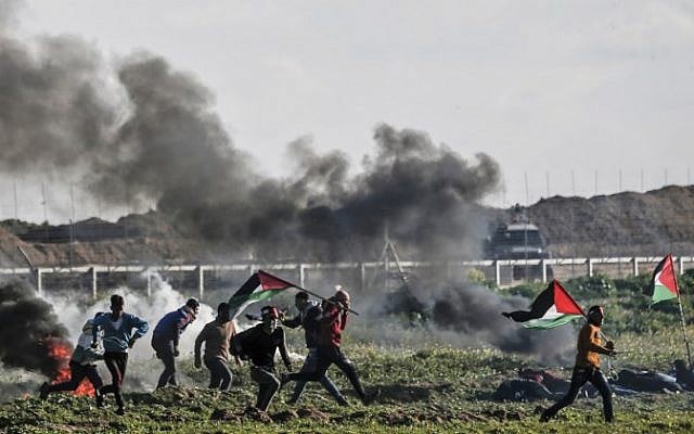 Palestinians holding Palestinian flags walk past burning tires during clashes near the security fence along the border with Israel, east of Gaza City, on February 22, 2019. (Mahmud Hams/AFP) Palestinians holding Palestinian flags walk past burning tires during clashes near the security fence along the border with Israel, east of Gaza City, on February 22, 2019. (Mahmud Hams/AFP)