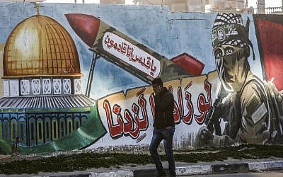 A Palestinian man walks past a mural depicting a masked fighter of the Qassam Brigades, the armed wing of the Hamas movement, next to a missile with a caption reading in Arabic "Oh Jerusalem, we are coming" and the Dome of the Rock, in a street in Rafah in the southern Gaza Strip on March 14, 2019. (Photo by SAID KHATIB / AFP)