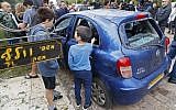 People gather around a damaged car next to the home of the Wolf family in the central Israeli village of Mishmeret, after it was hit by a rocket launched from Gaza, on March 25, 2019. The sign at left reads, 'Wolf family.' (Jack Guez/AFP)