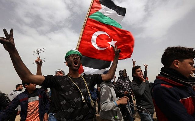 A Palestinian protester with black face-paint flashes the victory sign while marching with others flying Palestinian and Turkish national flags, during a demonstration marking the first anniversary of the "March of Return" protests, near the border with Israel east of Gaza City on March 30, 2019. (ANAS BABA / AFP) A Palestinian protester with black face-paint flashes the victory sign while marching with others flying Palestinian and Turkish national flags, during a demonstration marking the first anniversary of the "March of Return" protests, near the border with Israel east of Gaza City on March 30, 2019. (ANAS BABA / AFP)