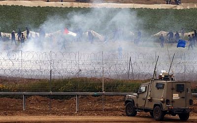 Israeli military vehicles keeping position at the border fence as Palestinians waving national flags demonstrate to mark the first anniversary of the 'March of Return' protests, March 30, 2019. (Jack Guez/AFP)