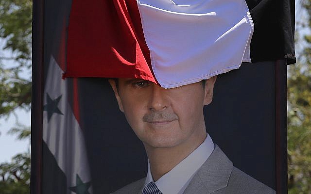 In this Aug. 13, 2018 file photo, a poster of Syrian President Bashar Assad, half-covered by a national flag, hangs at the border crossing point of Jdedeh Yabous, Syria. (AP Photo/Sergei Grits) In this Aug. 13, 2018 file photo, a poster of Syrian President Bashar Assad, half-covered by a national flag, hangs at the border crossing point of Jdedeh Yabous, Syria. (AP Photo/Sergei Grits)