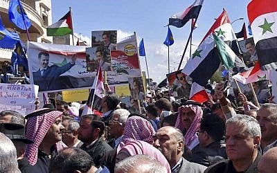 In this photo released by the Syrian official news agency SANA, Syrians hold national flags and portraits of Syrian President Bashar Assad during a protest against US President Donald Trump's move to recognize Israeli sovereignty over the Golan Heights, in Homs, Syria, on March 26, 2019. (SANA via AP)