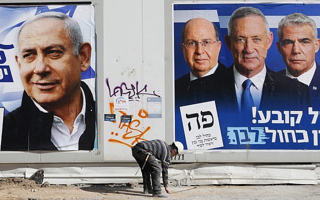 A laborer walks past electoral campaign posters in Tel Aviv, on April 3, 2019. ( JACK GUEZ / AFP)