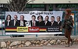 An Israeli Arab woman walks past a campaign poster showing Israeli-Arab candidates in Kafr Manda. (AHMAD GHARABLI / AFP)