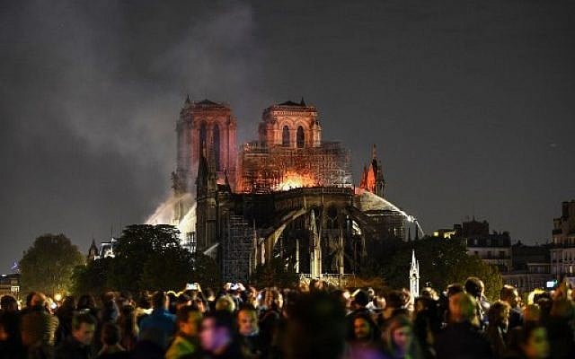 Bystanders look on as flames and smoke are seen billowing from the roof at Notre-Dame Cathedral in Paris on April 15, 2019. (ERIC FEFERBERG / AFP)
