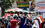 An Egyptian whirling dervish dances with a "tanoura" (multicolored skirt) as people gather with national flags outside polling stations during a referendum on constitutional amendments, at a school in the Haram district in the capital Cairo's western twin city of Giza, on the first day of a three-day poll, on April 20, 2019, with a poster showing President Abdel-Fattah al-Sissi next to slogans urging people to vote.  (MOHAMED EL-SHAHED / AFP)