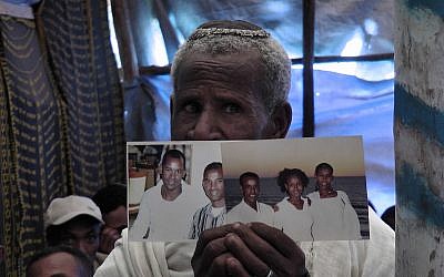 An Ethiopian worshiper at the synagogue in Addis Ababa praying and holding photos of family members living in Israel. (Bernard Dichek/Times of Israel)
