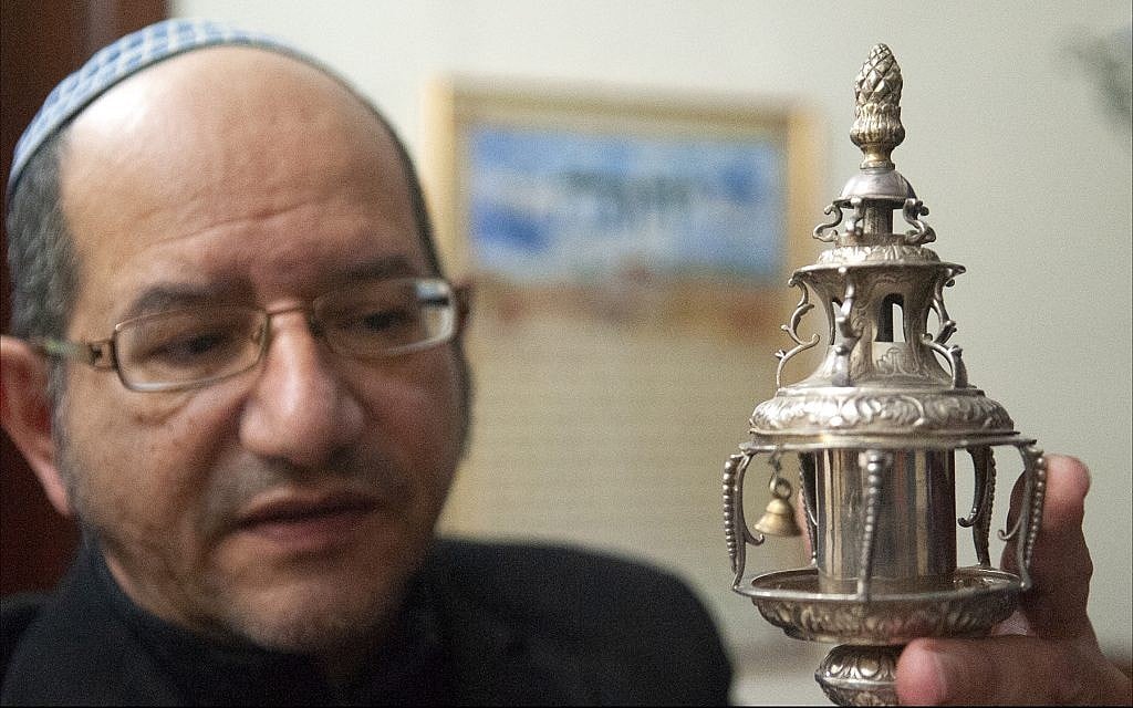 Reuven Ohayon, longtime leader of Malta’s tiny Jewish community, displays a silver ornament crowning a Libyan Torah scroll at the synagogue in Ta’Xbiex. (Larry Luxner/Times of Israel)