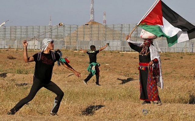 A Palestinian rioter hurls stones at Israeli troops as a woman wearing a traditional Palestinian outfit waves a national flag near the border with Israel, east of Gaza City, on May 10, 2019. (Photo by Said KHATIB / AFP) A Palestinian rioter hurls stones at Israeli troops as a woman wearing a traditional Palestinian outfit waves a national flag near the border with Israel, east of Gaza City, on May 10, 2019. (Photo by Said KHATIB / AFP)