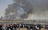 Palestinian protesters riot along the security fence east of Gaza City as smoke billows from fields across the fence caused by an incendiary device attached to a kite and flown across the border into Israel from the Gaza Strip, on May 15, 2019. (MAHMUD HAMS / AFP)
