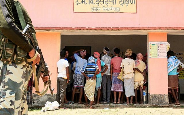 Indian voters queue to cast their votes as a CRPF personnel (L) stands guard at Shikaripara area in the Dumka district of Jharkhand state on May 19, 2019, during the 7th and final phase of India's general election. (Sanjib DUTTA / AFP)