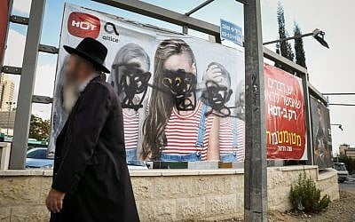 An ultra-Orthodox Jewish man walks past a vandalized billboard in Jerusalem where women's faces have been blotted out, November 2, 2017. (Noam Revkin Fenton/Flash90)