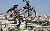 Taiwanese cyclist and world traveler Jacky Chen poses while lifting his bicycle on the Mount of Olives overlooking the Old City of Jerusalem and the Dome of the Rock on June 10, 2019. (Photo by MENAHEM KAHANA / AFP)