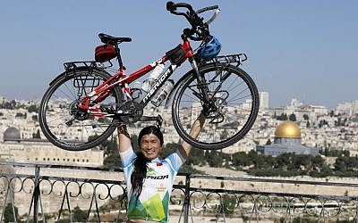 Taiwanese cyclist and world traveler Jacky Chen poses while lifting his bicycle on the Mount of Olives overlooking the Old City of Jerusalem and the Dome of the Rock on June 10, 2019. (Photo by MENAHEM KAHANA / AFP)