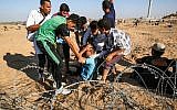 Illustrative: Palestinian protesters assist an injured protester during clashes with Israeli forces across the barbed-wire fence during a border demonstration near Rafah in the southern Gaza Strip on July 19, 2019. (SAID KHATIB / AFP)