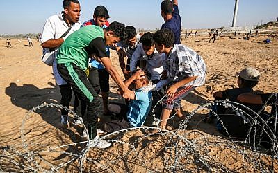 Illustrative: Palestinian protesters assist an injured protester during clashes with Israeli forces across the barbed-wire fence during a border demonstration near Rafah in the southern Gaza Strip on July 19, 2019. (SAID KHATIB / AFP)