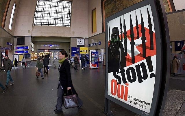 People walk by a poster from the right-wing Swiss People's Party (SVP/UDC) depicting a woman wearing a burqa in front of a Swiss flag upon which are minarets which resemble missiles, at the central station in Geneva, Switzerland, November 4, 2009. (Salvatore Di Nolfi/Keystone/AP) People walk by a poster from the right-wing Swiss People's Party (SVP/UDC) depicting a woman wearing a burqa in front of a Swiss flag upon which are minarets which resemble missiles, at the central station in Geneva, Switzerland, November 4, 2009. (Salvatore Di Nolfi/Keystone/AP)