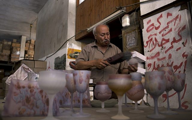 Abed Abu Sedou, removes the dust from samples of hand-painted glasses displayed on a table in his closed glass factory in Gaza City, July 6, 2019. (Khalil Hamra/AP) Abed Abu Sedou, removes the dust from samples of hand-painted glasses displayed on a table in his closed glass factory in Gaza City, July 6, 2019. (Khalil Hamra/AP)