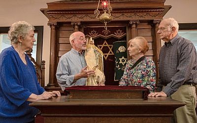 The members of Temple Mishkan Israel — from left, Hanna Berger, Ronnie Leet, Joanie Gibian Looney and Charles Pollack — stand in front of the Torah ark. The synagogue has not held weekly services for decades. (Amy Milligan via JTA)