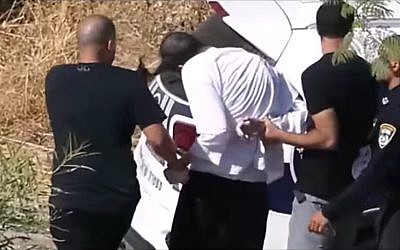 A police officer is seen pulling an ultra-Orthodox man's sidelocks, during a protest in Beit Shemesh, on July 6, 2019. (Facebook screenshot)