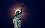 A full moon rises behind the Statue of Liberty in New York City, on May 18, 2019.  (Photo by Johannes EISELE / AFP)