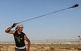 A Palestinian rioter uses a slingshot to hurl stones at Israeli forces near the fence along the border with Israel in the eastern Gaza Strip on August 16, 2019. (Photo by MAHMUD HAMS / AFP)