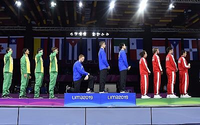 In this August 9, 2019 photo, released by Lima 2019 News Services, Race Imboden of the United States takes a knee, as teammates Mick Itkin and Gerek Meinhardt stand on the podium after winning the gold medal in team's foil, at the Pan American Games in Lima, Peru. (Jose Sotomayor/Lima 2019 News Services via AP)