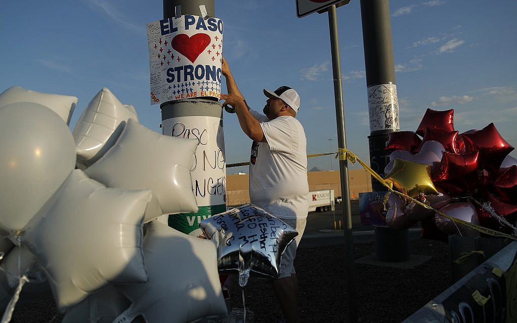 A man hangs up an "El Paso Strong" sign at a makeshift memorial at the scene of a mass shooting at a shopping complex, August 6, 2019, in El Paso, Texas. (AP Photo/John Locher)