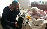 Illustrative: Krystyna Danko receives flowers from From the Depths founder Jonny Daniels in her Warsaw apartment on her 102nd birthday, July 9, 2019. (From the Depths via JTA)