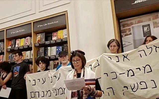A demonstrator speaks at a Jewish protest against Amazon at one of the company’s brick-and-mortar stores in New York City, Aug. 11, 2019. The protest was held on Tisha B’Av, a traditional Jewish day of mourning. Behind the speaker is a banner with a Hebrew quotation from the Book of Lamentations. (Screenshot from Facebook video via JTA) A demonstrator speaks at a Jewish protest against Amazon at one of the company’s brick-and-mortar stores in New York City, Aug. 11, 2019. The protest was held on Tisha B’Av, a traditional Jewish day of mourning. Behind the speaker is a banner with a Hebrew quotation from the Book of Lamentations. (Screenshot from Facebook video via JTA)