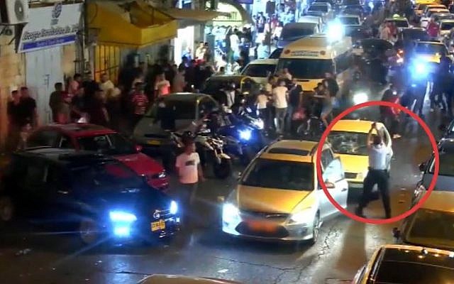 A police officer (marked by red circle) fires in the air to scatter several young men attacking a Jewish driver on Salah Ad-Din Street in East Jerusalem, August 11, 2019. (Israel Police video) A police officer (marked by red circle) fires in the air to scatter several young men attacking a Jewish driver on Salah Ad-Din Street in East Jerusalem, August 11, 2019. (Israel Police video)