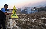 A man fixes a Hezbollah flag at the 'Garden of Iran' Park in the Lebanese village of Maroun al-Ras on September 1, 2019, as fires blaze on the Lebanese side along the border following an exchange of fire with Israel. (Mahmoud Zayyat/AFP)