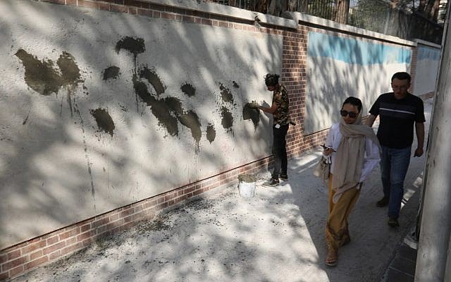 Iranians walk past a mural painting, partially covered with cement, on the wall of the former US embassy in the capital Tehran on September 29, 2019. (ATTA KENARE / AFP) Iranians walk past a mural painting, partially covered with cement, on the wall of the former US embassy in the capital Tehran on September 29, 2019. (ATTA KENARE / AFP)