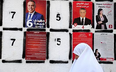 In this September 4, 2019 file photo, a woman walks past a wall of campaign posters in Tunis, Tunisia. (AP Photo/Hassene Dridi, File)