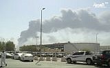 In this image made from a video broadcast on the Saudi-owned Al-Arabiya satellite news channel on September 14, 2019, a man walks through a parking lot as the smoke from a fire at the Abqaiq oil processing facility can be seen behind him in Buqyaq, Saudi Arabia. (Al-Arabiya via AP)