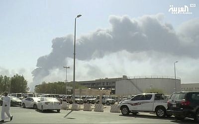 In this image made from a video broadcast on the Saudi-owned Al-Arabiya satellite news channel on September 14, 2019, a man walks through a parking lot as the smoke from a fire at the Abqaiq oil processing facility can be seen behind him in Buqyaq, Saudi Arabia. (Al-Arabiya via AP)
