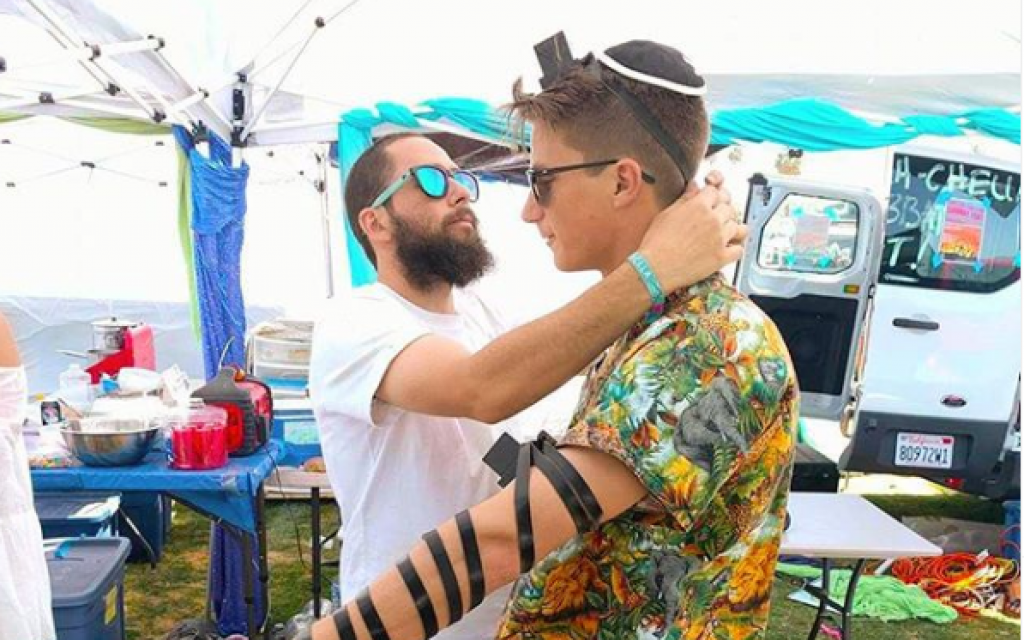 Rabbi Daniel Bortz helps a Coachella music festival attendee put on phylacteries and pray. (Courtesy)